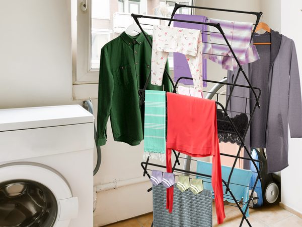 Black 3-tier clothes airer with shirts on hangers and towels on the lower tiers, in a utility room next to a washing machine and outside on a patio