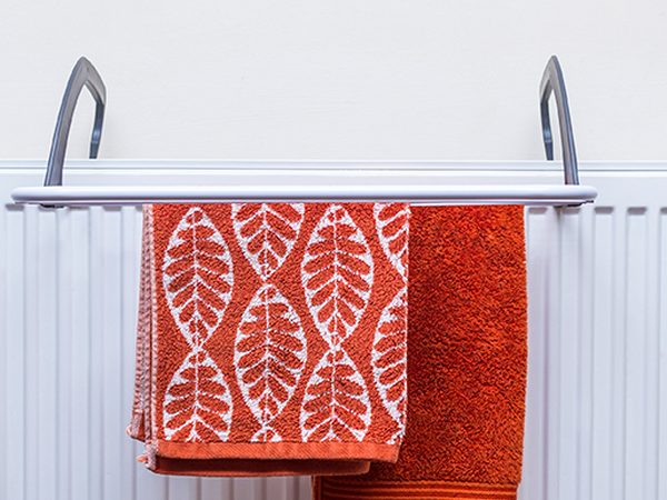 Over-radiator clothes airer hooked onto a white radiator with two orange hand towels drying on it